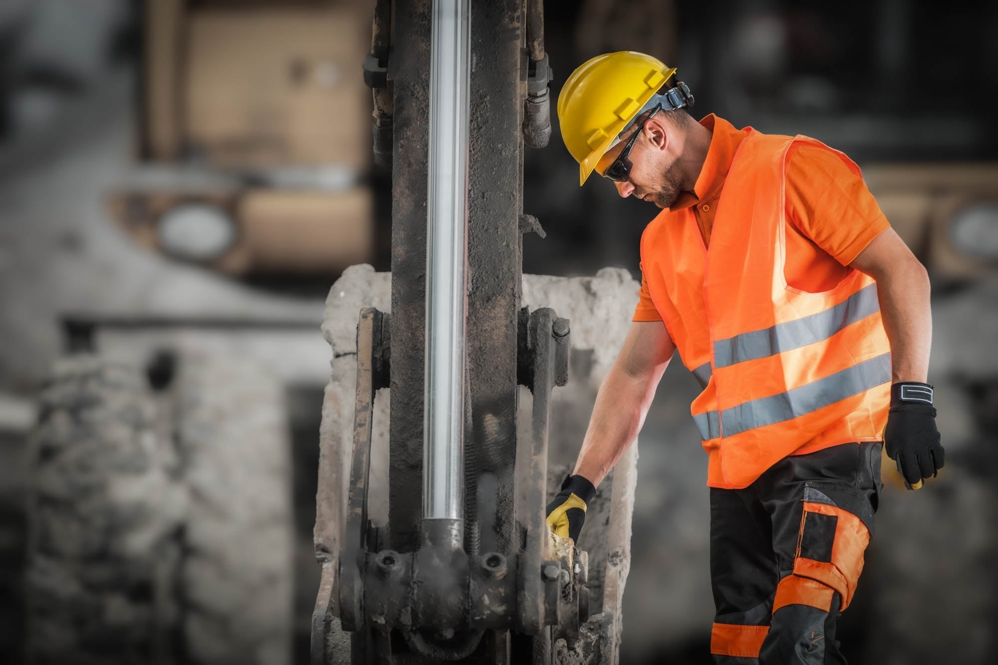 Construction worker operating heavy equipment on a jobsite — lead dust from drilling, demolition, and old materials travels home on work clothes, boots, and skin, putting families at risk without anyone realizing it