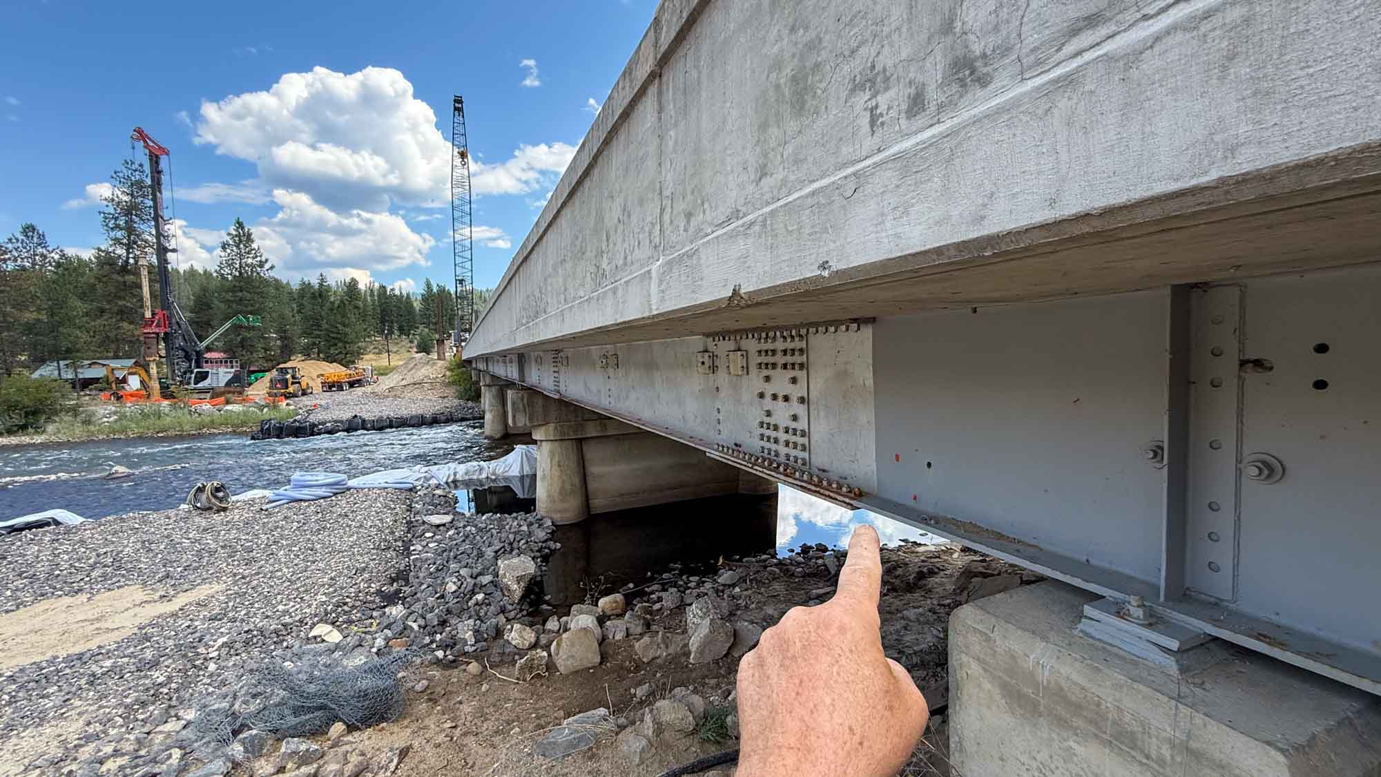 Hand pointing to a bridge structure during a road trip stop — older bridges and overpasses are coated in lead paint that weathers and flakes into the soil and waterways below